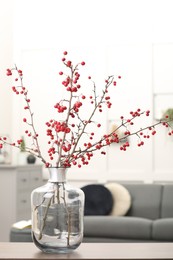 Photo of Hawthorn branches with red berries on table in living room