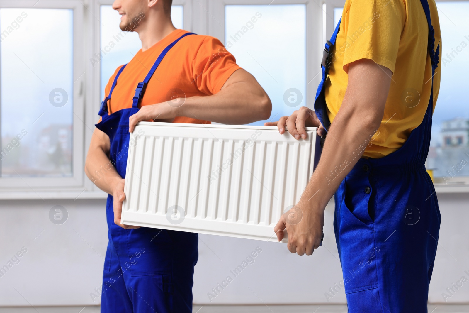Photo of Professional plumbers with new heating radiator indoors, closeup
