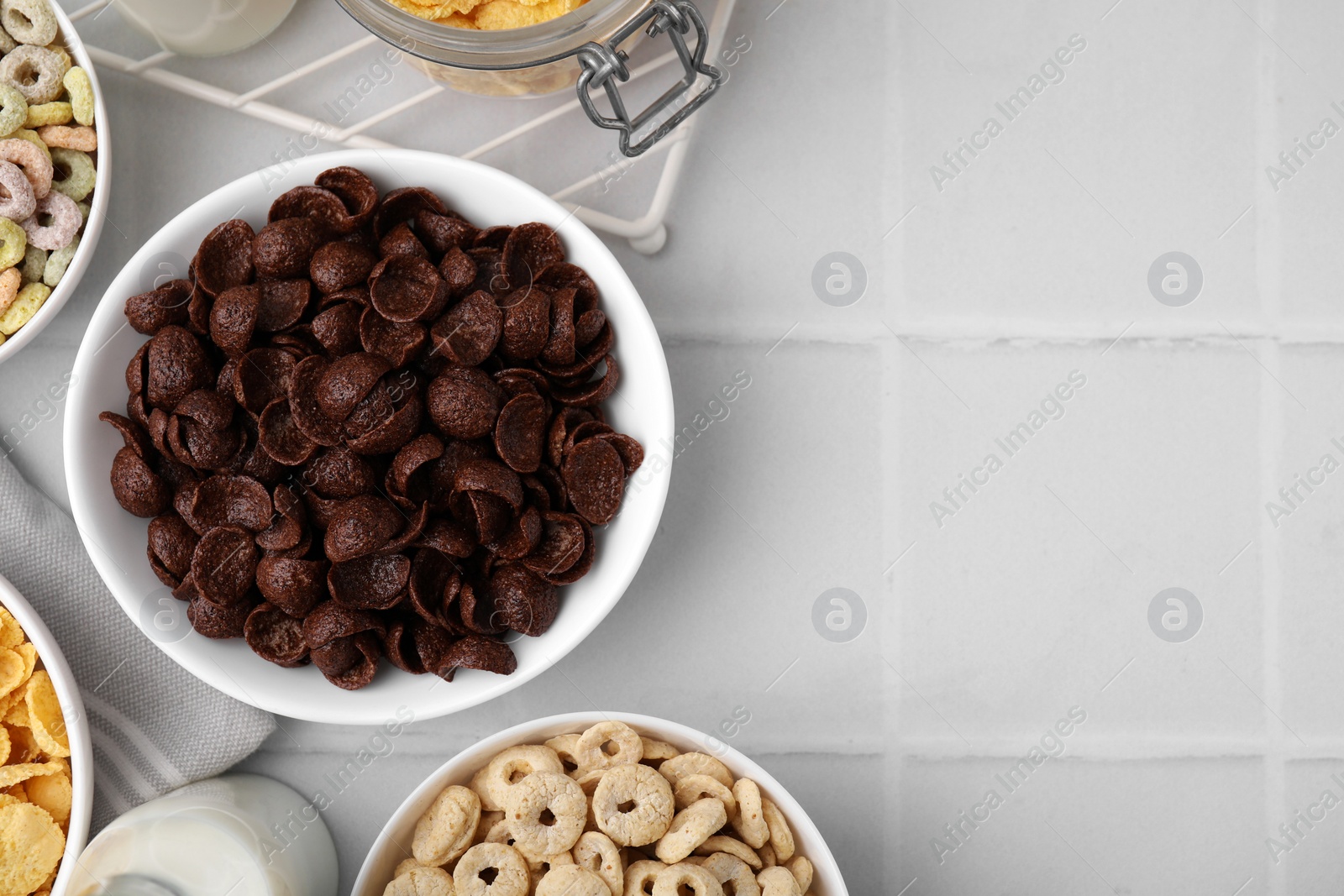 Photo of Different delicious breakfast cereals and milk on white tiled table, flat lay. Space for text