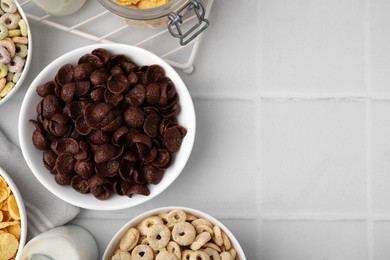 Photo of Different delicious breakfast cereals and milk on white tiled table, flat lay. Space for text