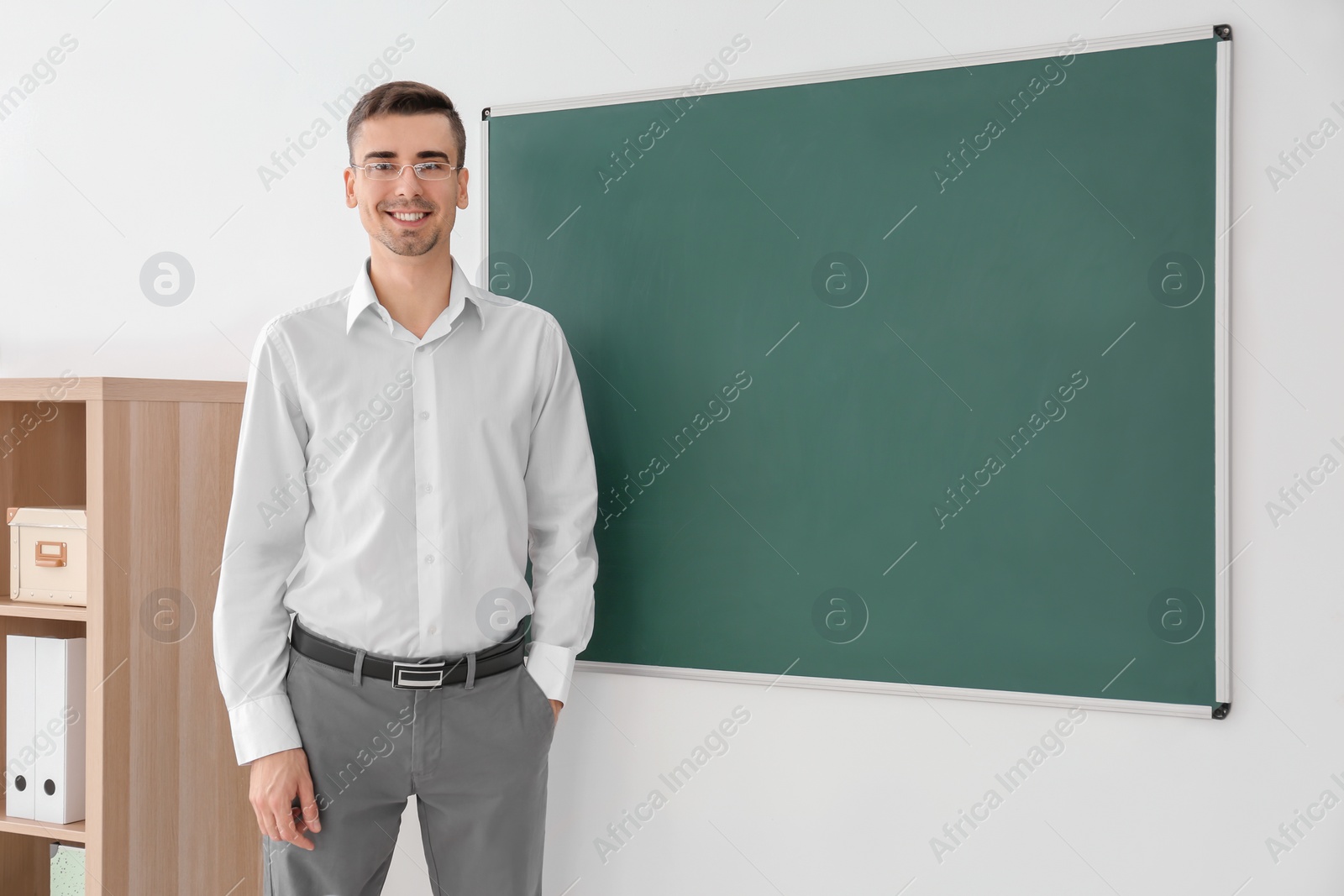 Photo of Young male teacher standing near blackboard in classroom