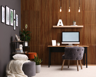 Comfortable workplace with computer near wooden wall in stylish room interior. Home office design