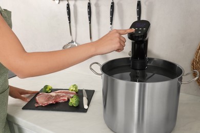 Woman using thermal immersion circulator in kitchen, closeup. Sous vide cooking