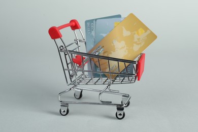 Photo of Small metal shopping cart with credit cards on light background