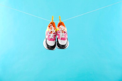 Stylish sneakers drying on washing line against light blue background