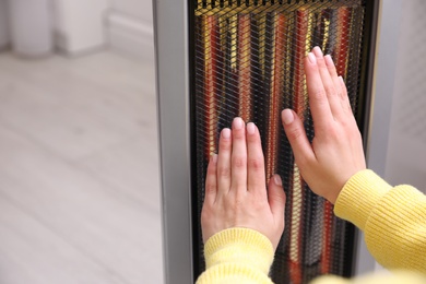 Photo of Woman warming hands near heater indoors, closeup