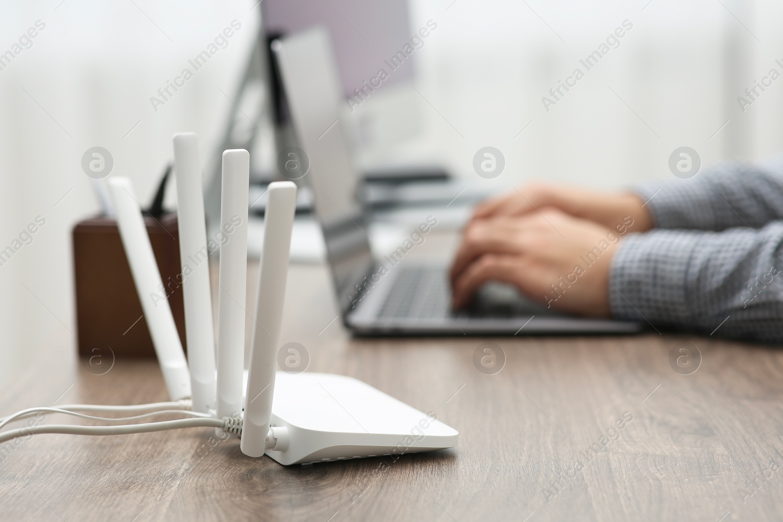 Photo of Man with laptop working at wooden table indoors, focus of Wi-Fi router