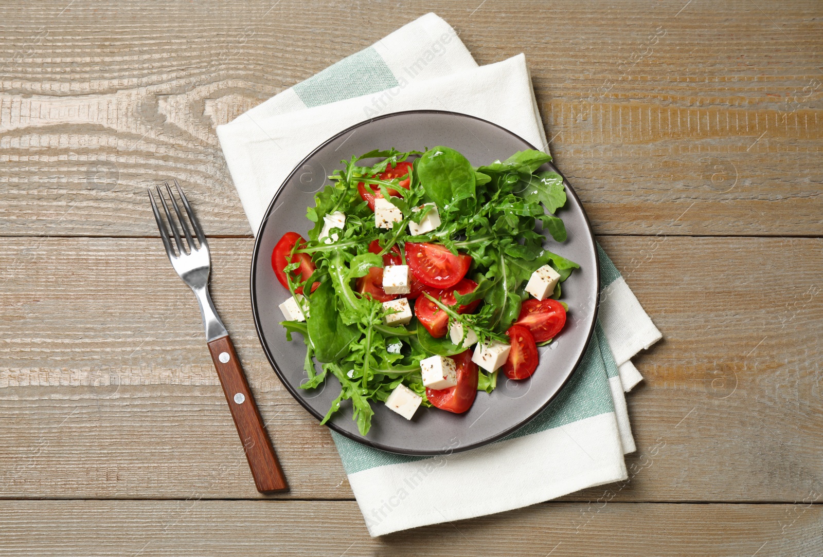 Photo of Delicious salad with feta cheese, arugula and tomatoes on wooden table, flat lay