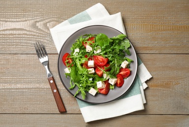 Delicious salad with feta cheese, arugula and tomatoes on wooden table, flat lay