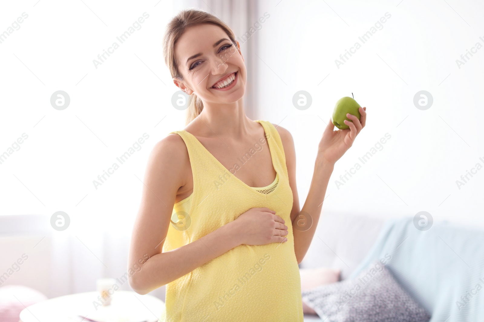 Photo of Young pregnant woman holding apple at home