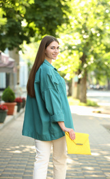 Beautiful young woman with elegant envelope bag outdoors on summer day