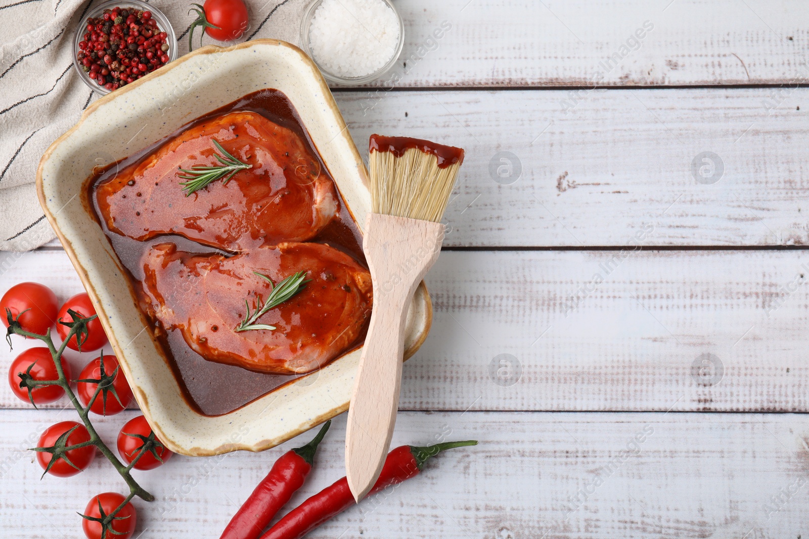 Photo of Flat lay composition with raw marinated meat in baking dish, products and basting brush on white wooden table. Space for text