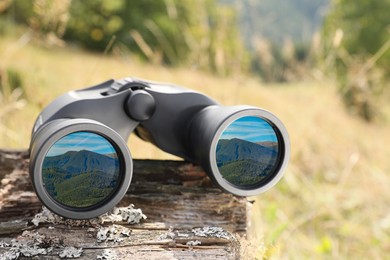 Binoculars on wooden log outdoors. Mountain landscape reflecting in lenses