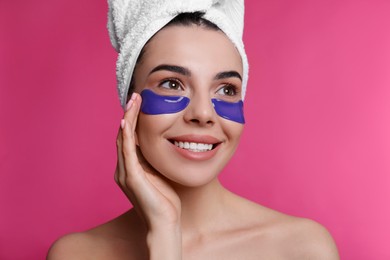 Photo of Beautiful young woman with under eye patches and hair wrapped in towel on pink background