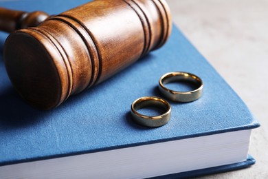 Photo of Divorce concept. Wooden gavel, wedding rings and book on grey table, closeup