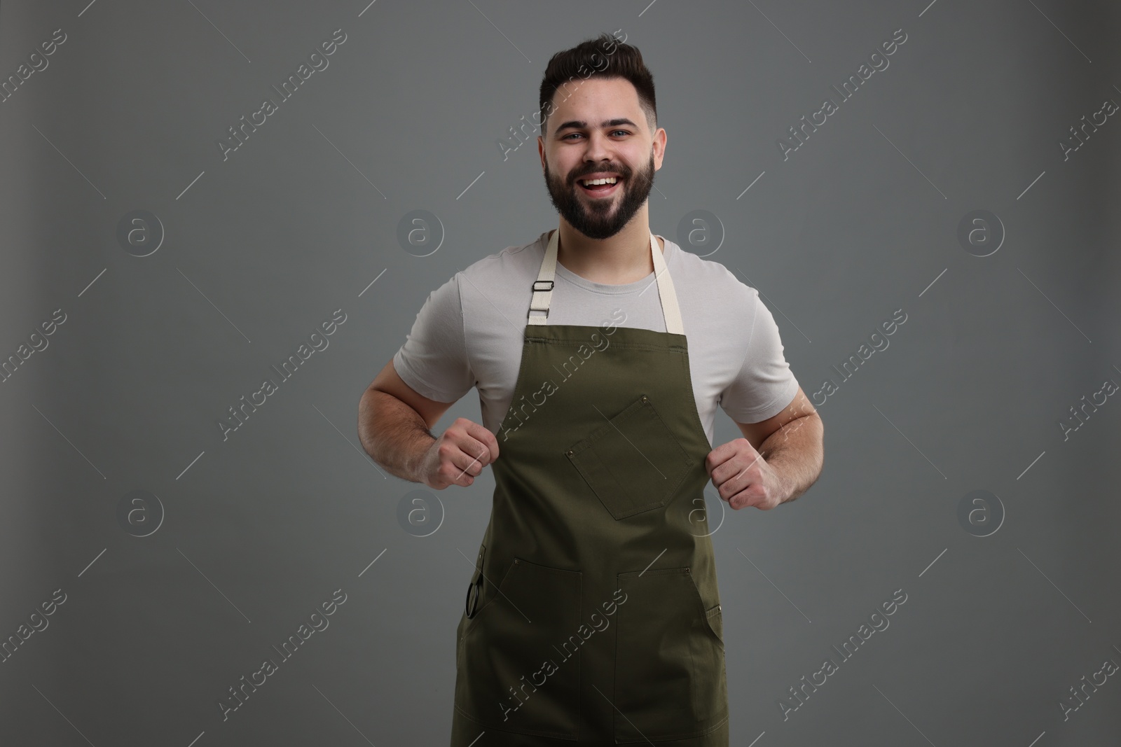 Photo of Smiling man in kitchen apron on grey background. Mockup for design