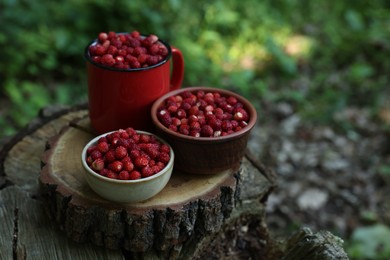 Dishes with tasty wild strawberries on stump against blurred background, closeup. Space for text