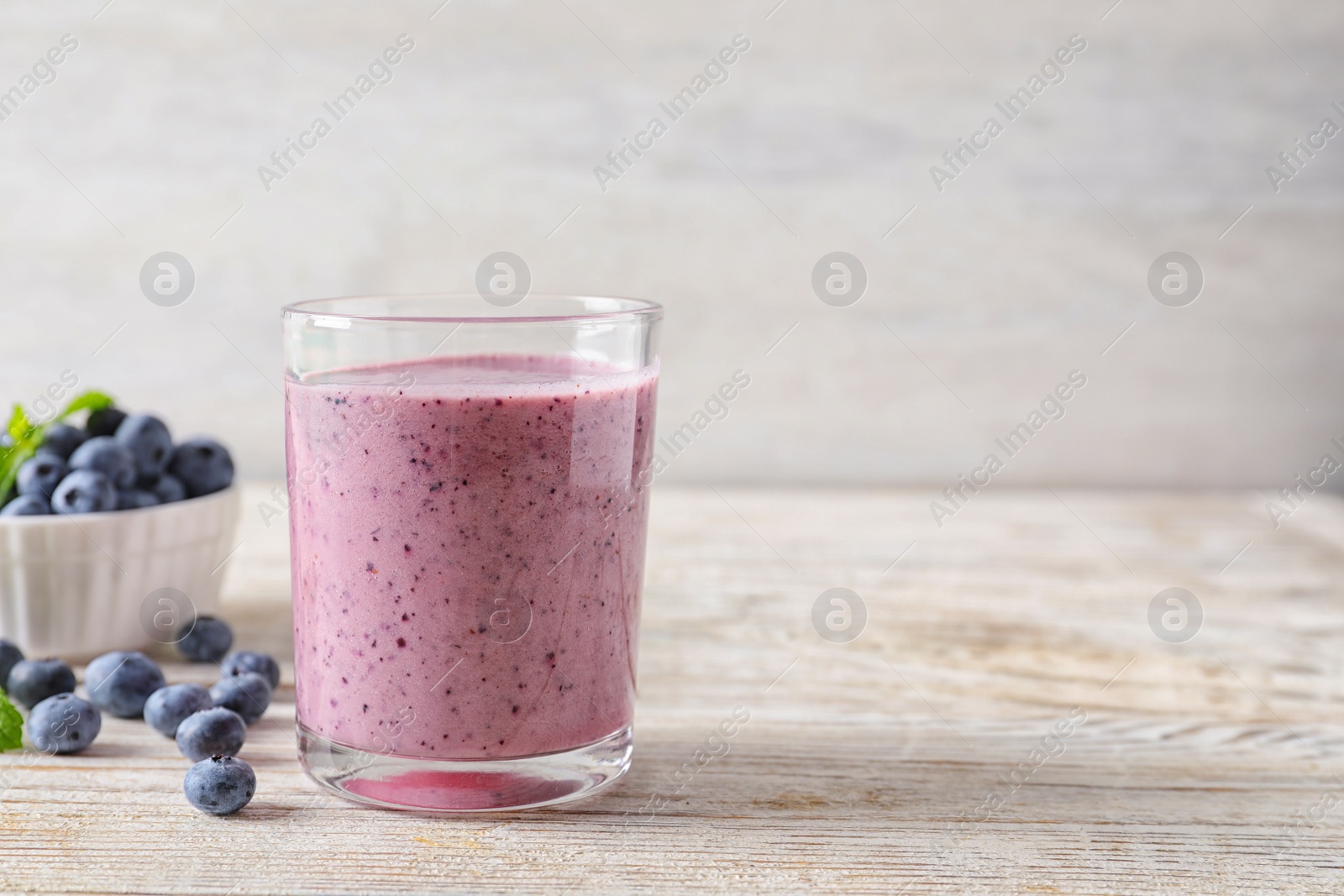 Photo of Tasty blueberry smoothie in glass, bowl with berries on table against light background with space for text