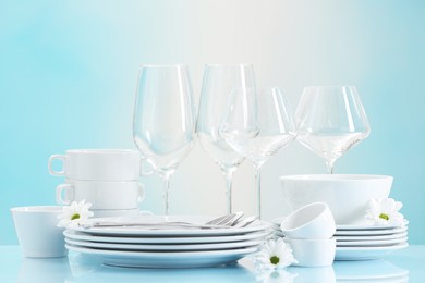 Photo of Set of many clean dishware, cutlery, flowers and glasses on light blue table