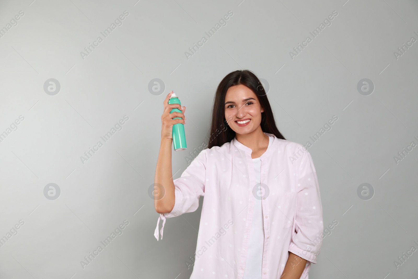 Photo of Woman applying dry shampoo onto her hair on light grey background. Space for text