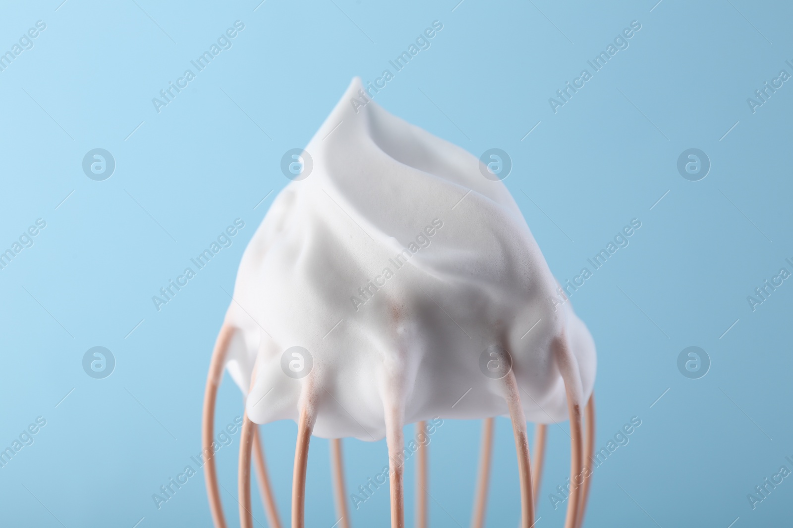 Photo of Whisk with whipped cream on light blue background, closeup