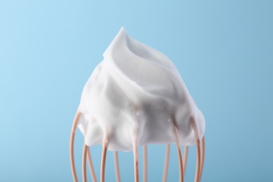 Whisk with whipped cream on light blue background, closeup