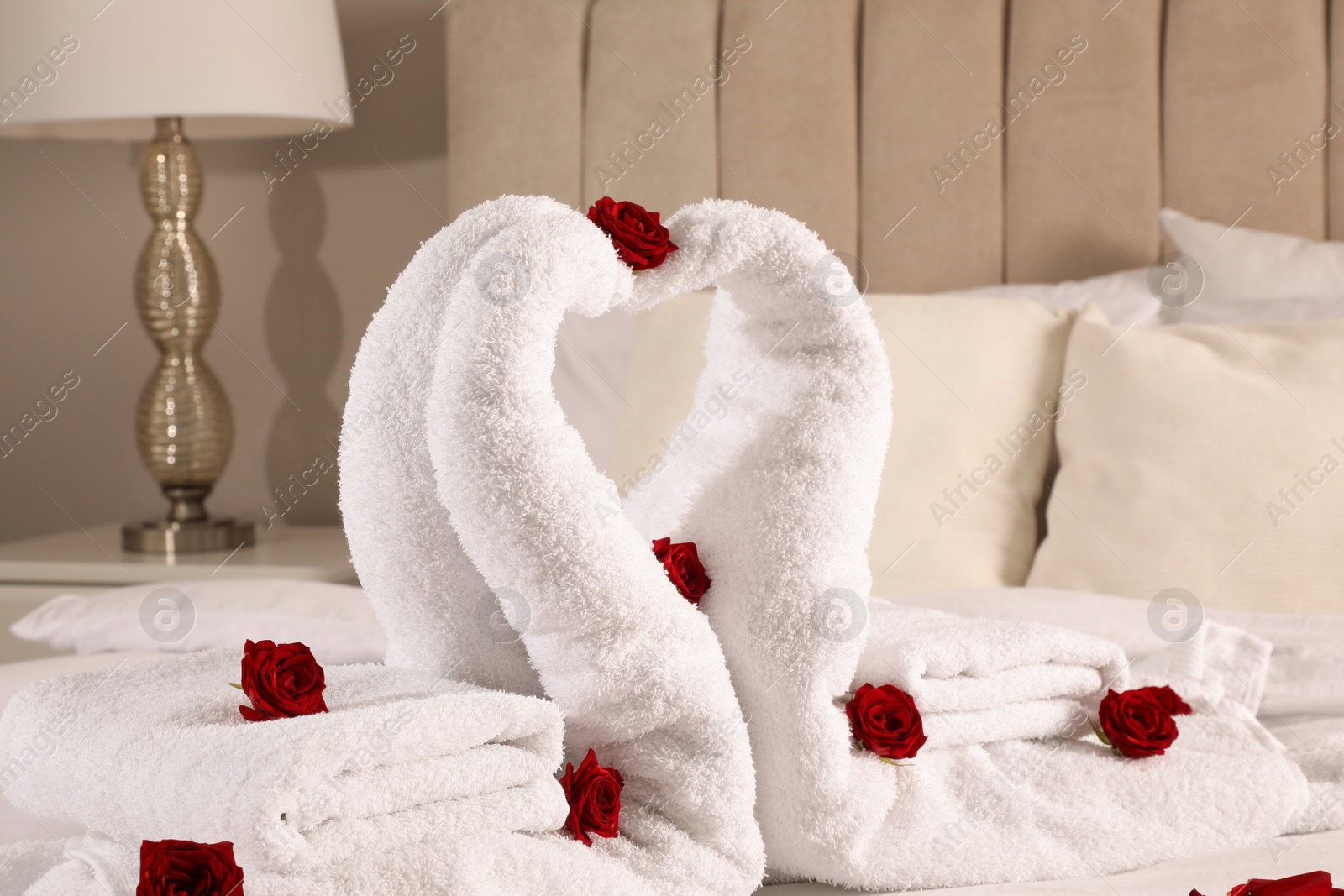 Photo of Beautiful swans made of towels decorated with red roses on bed in room, closeup