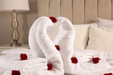 Photo of Beautiful swans made of towels decorated with red roses on bed in room, closeup