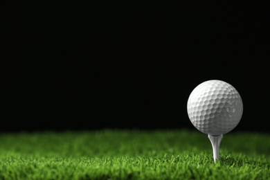 Photo of Golf ball with tee on artificial grass against black background, space for text