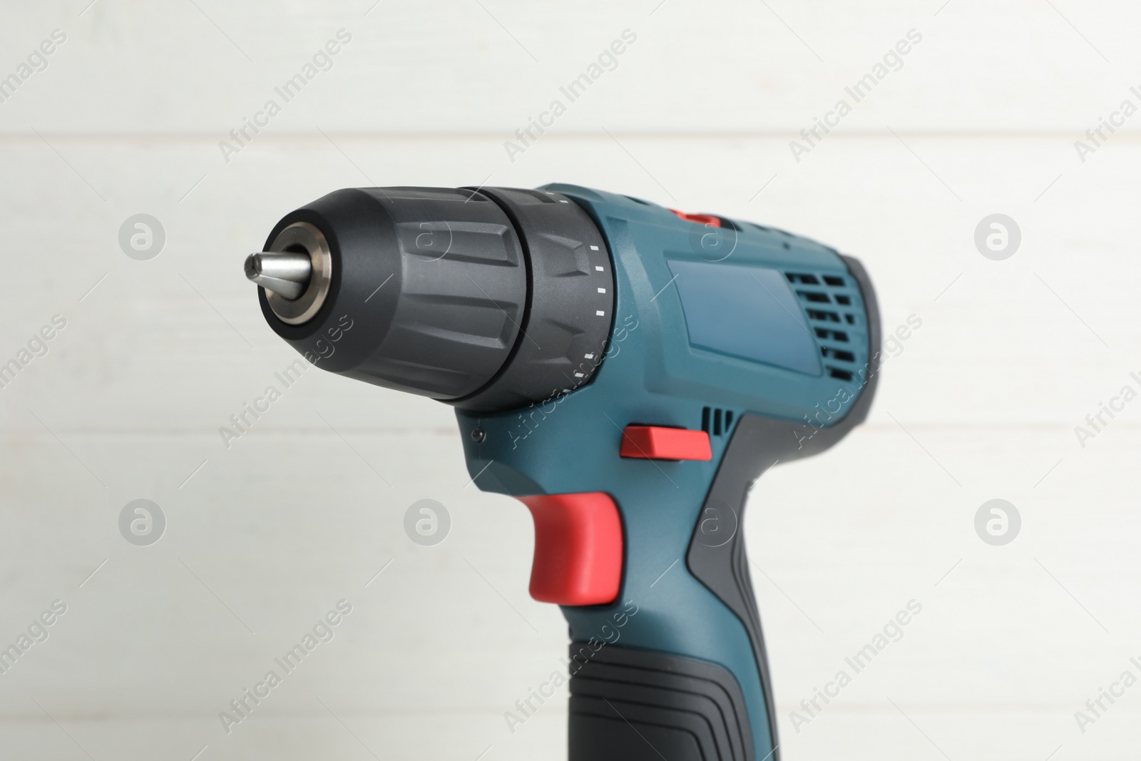 Photo of Modern electric power drill near white wooden wall, closeup