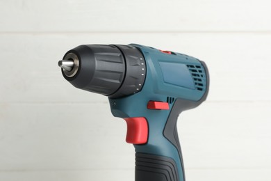 Photo of Modern electric power drill near white wooden wall, closeup