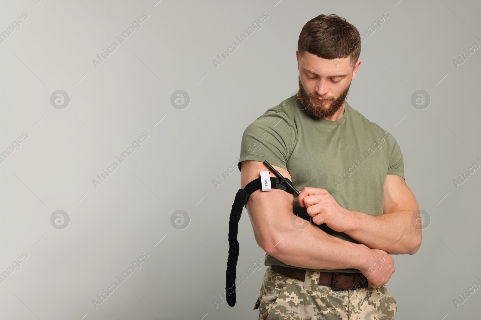 Photo of Soldier in military uniform applying medical tourniquet on arm against light grey background. Space for text