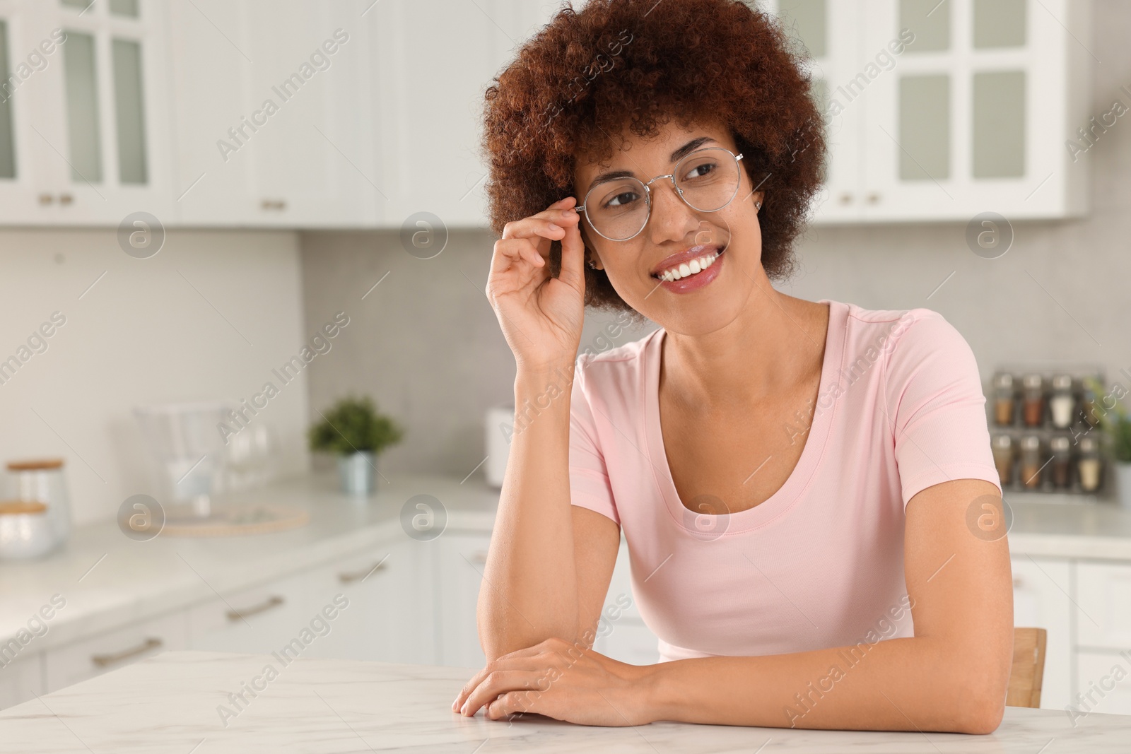 Photo of Happy young woman with eyeglasses at table in kitchen. Space for text