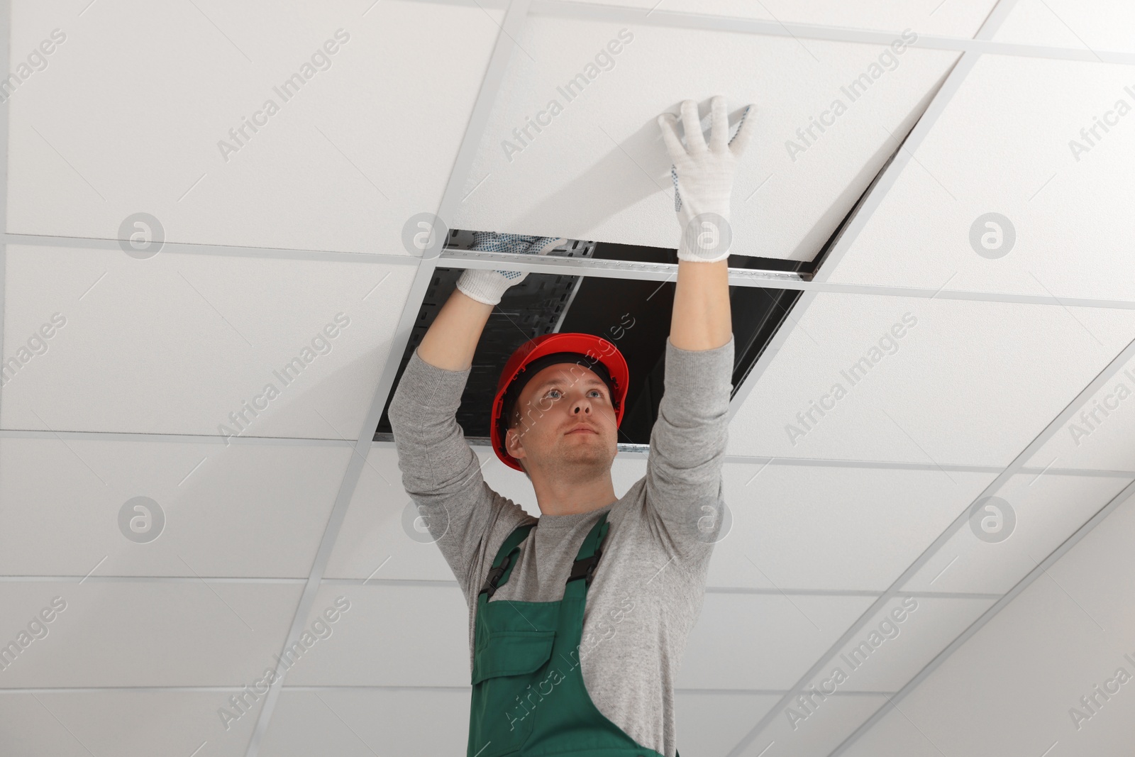 Photo of Suspended ceiling installation. Builder working with PVC tile
