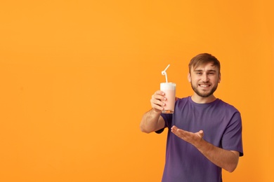 Photo of Young man with glass of delicious milk shake on color background