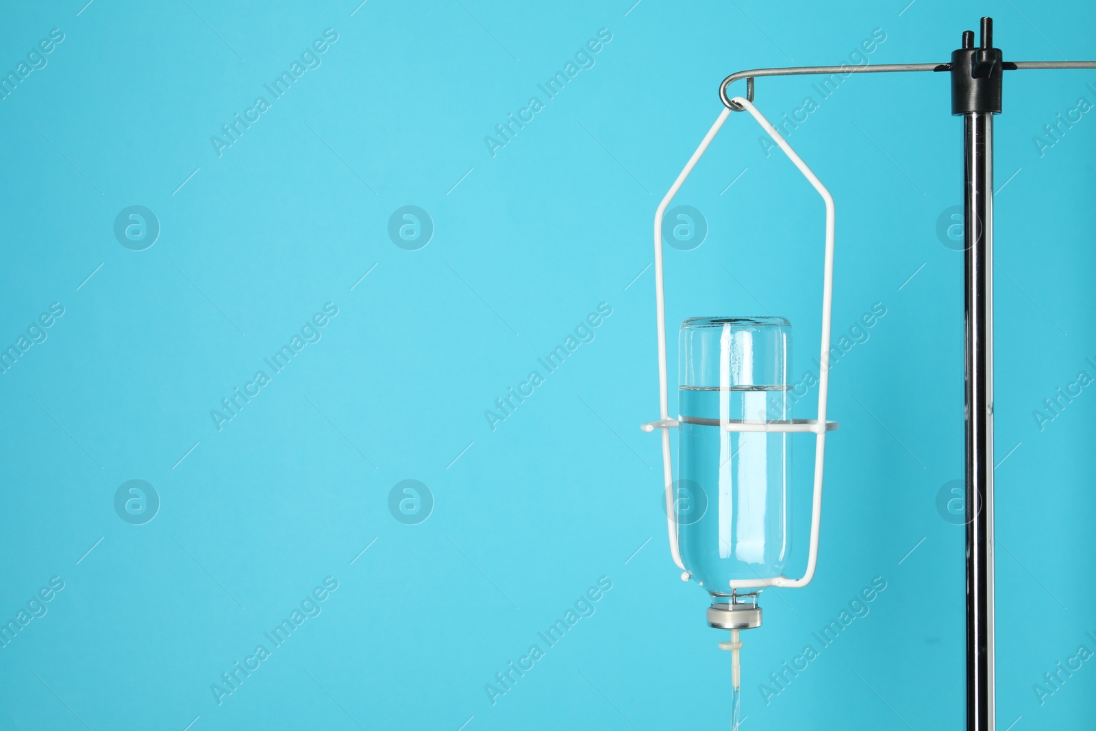 Photo of IV infusion set on pole against light blue background. Space for text