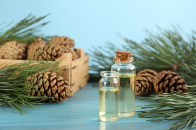 Pine essential oil, cones and branches on light blue wooden table