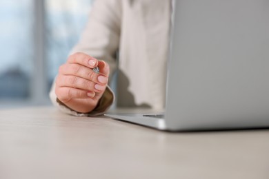 Woman with pen working on laptop at wooden table, closeup. Electronic document management