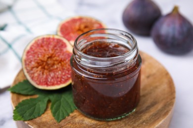 Photo of Glass jar of tasty sweet fig jam and fruits on white table, closeup