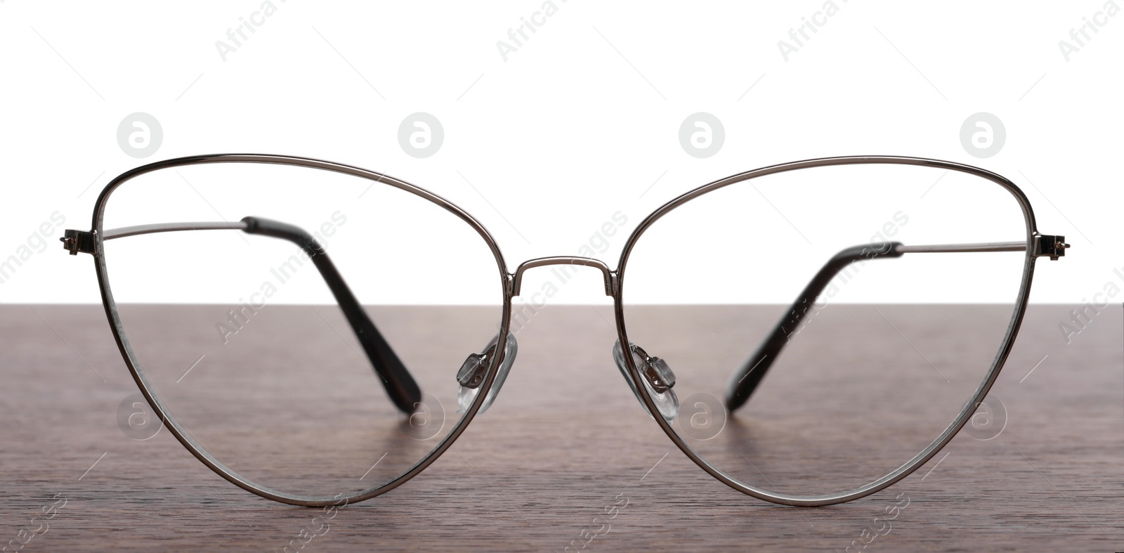 Photo of Stylish glasses with metal frame on wooden table against white background