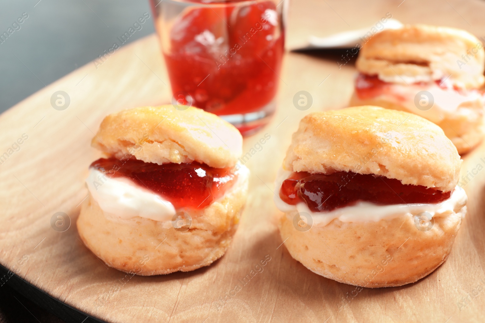 Photo of Tasty scones with clotted cream and jam on wooden plate, closeup