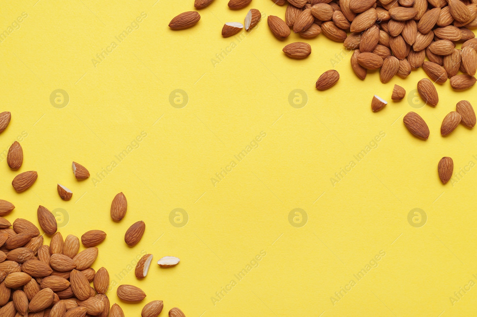 Photo of Delicious raw almonds on yellow background, flat lay. Space for text