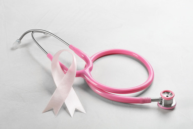 Photo of Pink ribbon and stethoscope on light grey stone background. Breast cancer concept