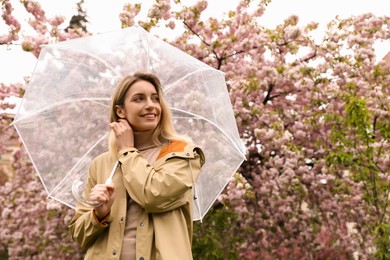 Young woman with umbrella near blossoming tree on spring day