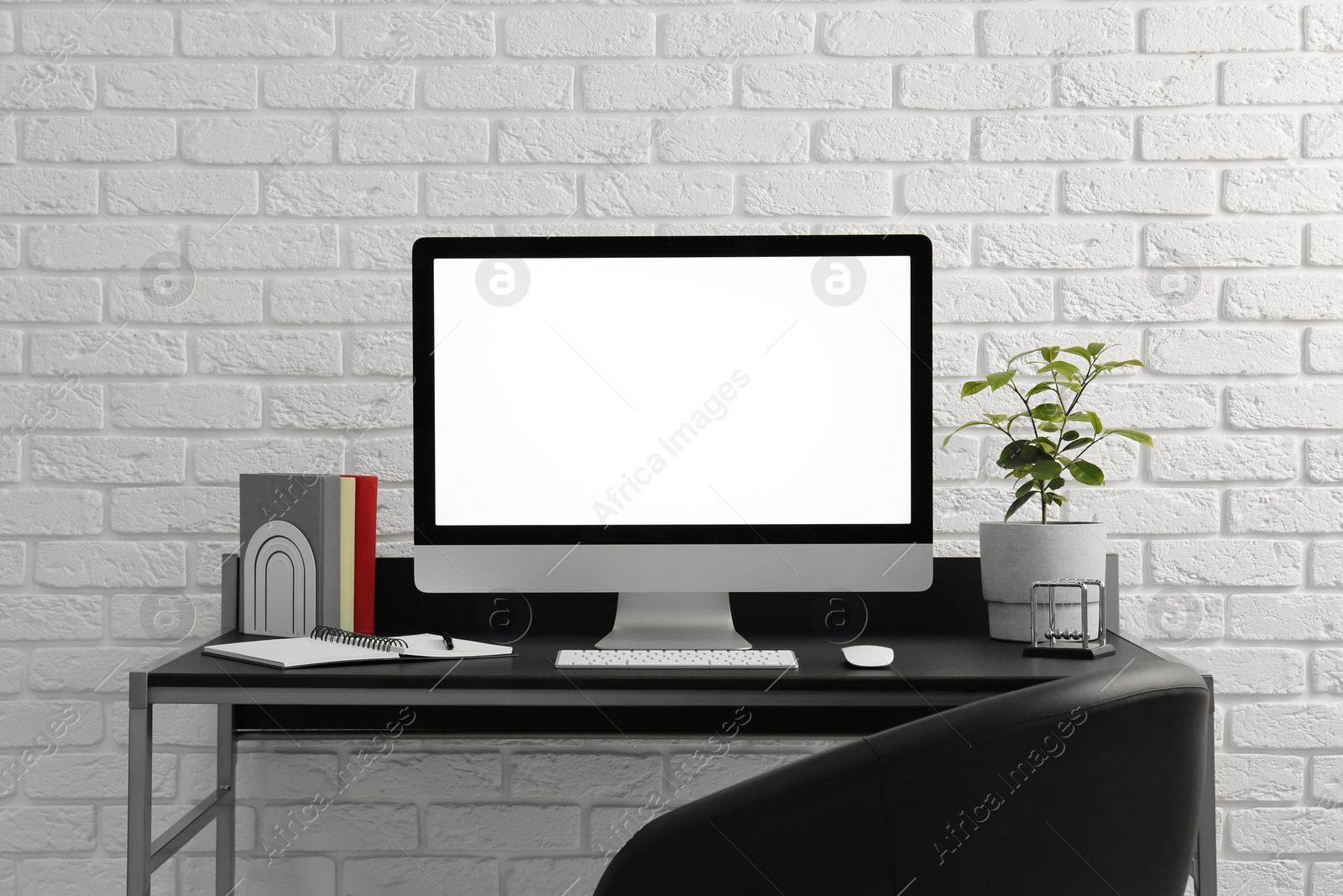 Photo of Stylish workplace with computer, houseplant and stationery on table near white brick wall