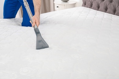 Photo of Man disinfecting mattress with vacuum cleaner, closeup. Space for text