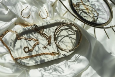 Photo of Metal chains and other different accessories on white fabric, flat lay. Luxury jewelry