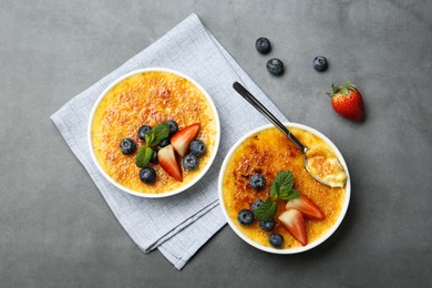 Delicious creme brulee with berries and mint in bowls on grey table, flat lay