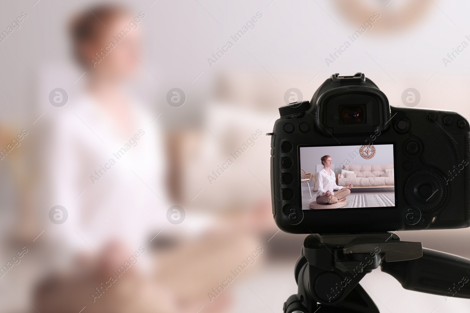 Image of Woman meditating on wicker mat at home, selective focus on camera display