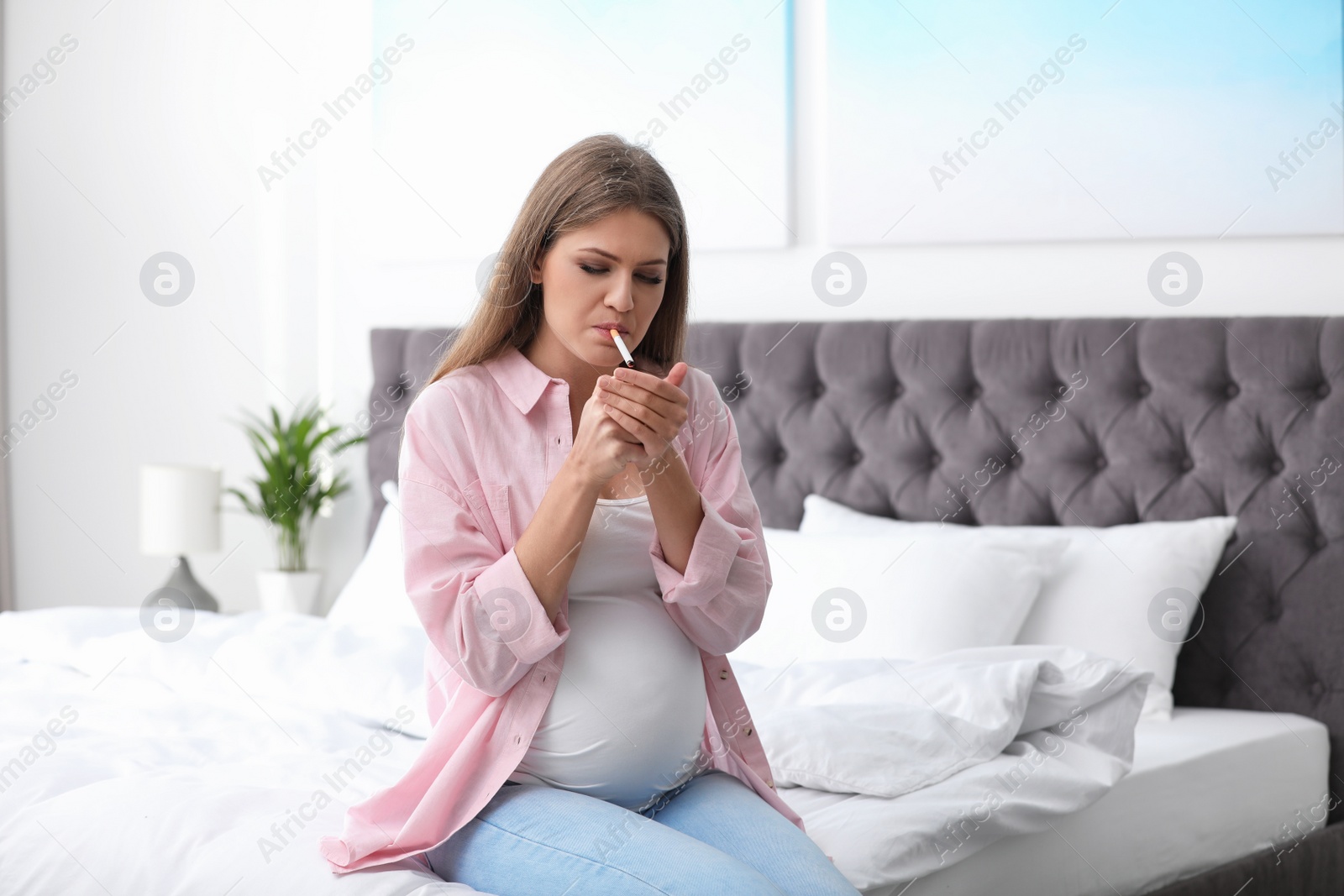 Photo of Young pregnant woman smoking cigarette in bedroom. Harm to unborn baby